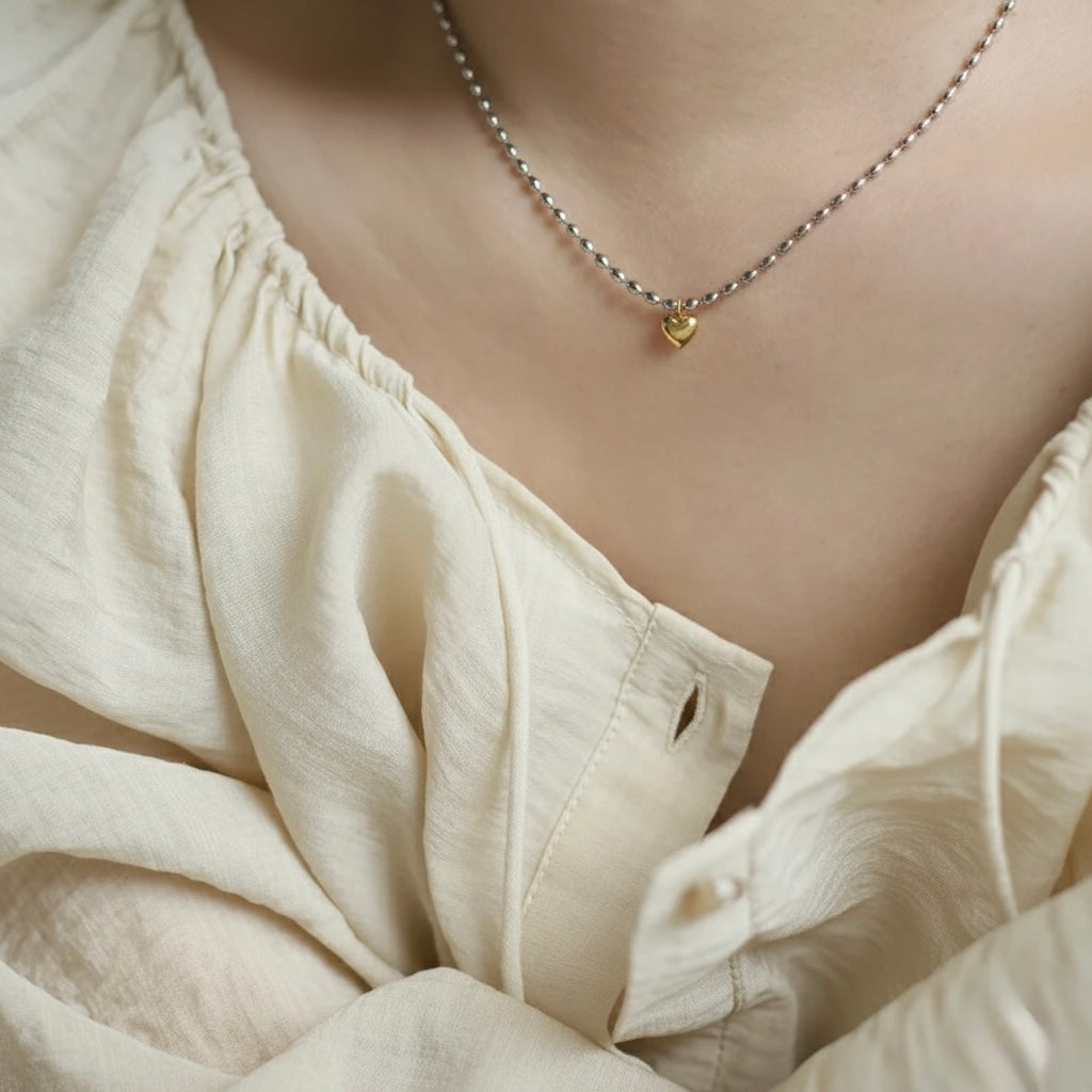 Necklace with a heart pendant worn by a person in a light-colored top.