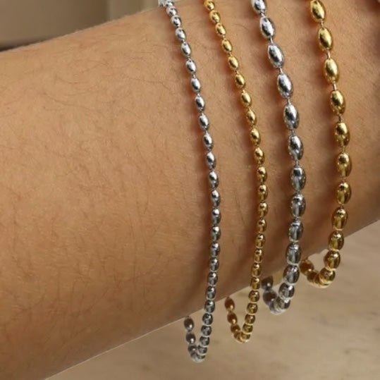 beaded Bracelet, one silver and one gold, draped over a person's arm.