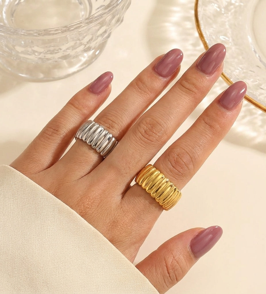 Hand wearing two rings with pink nail polish on a neutral background
