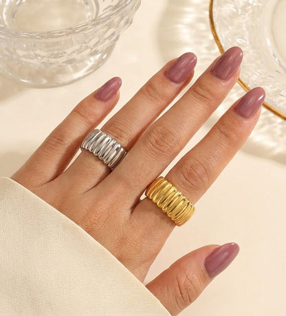 Hand wearing two rings with pink nail polish on a neutral background