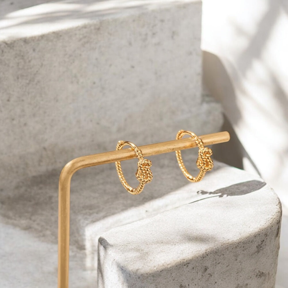 Gold hoop earrings on a marble surface with a gold stand.