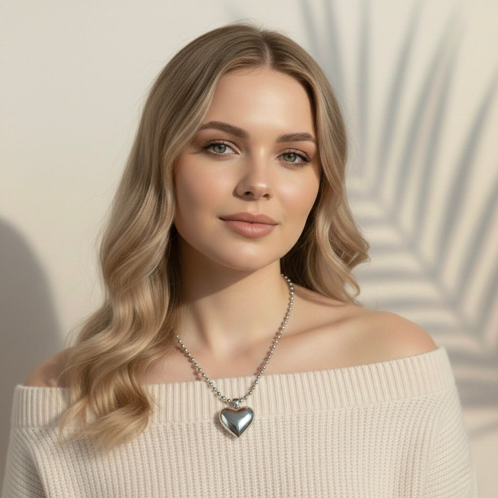 Woman wearing a silver heart-shaped necklace against a neutral background