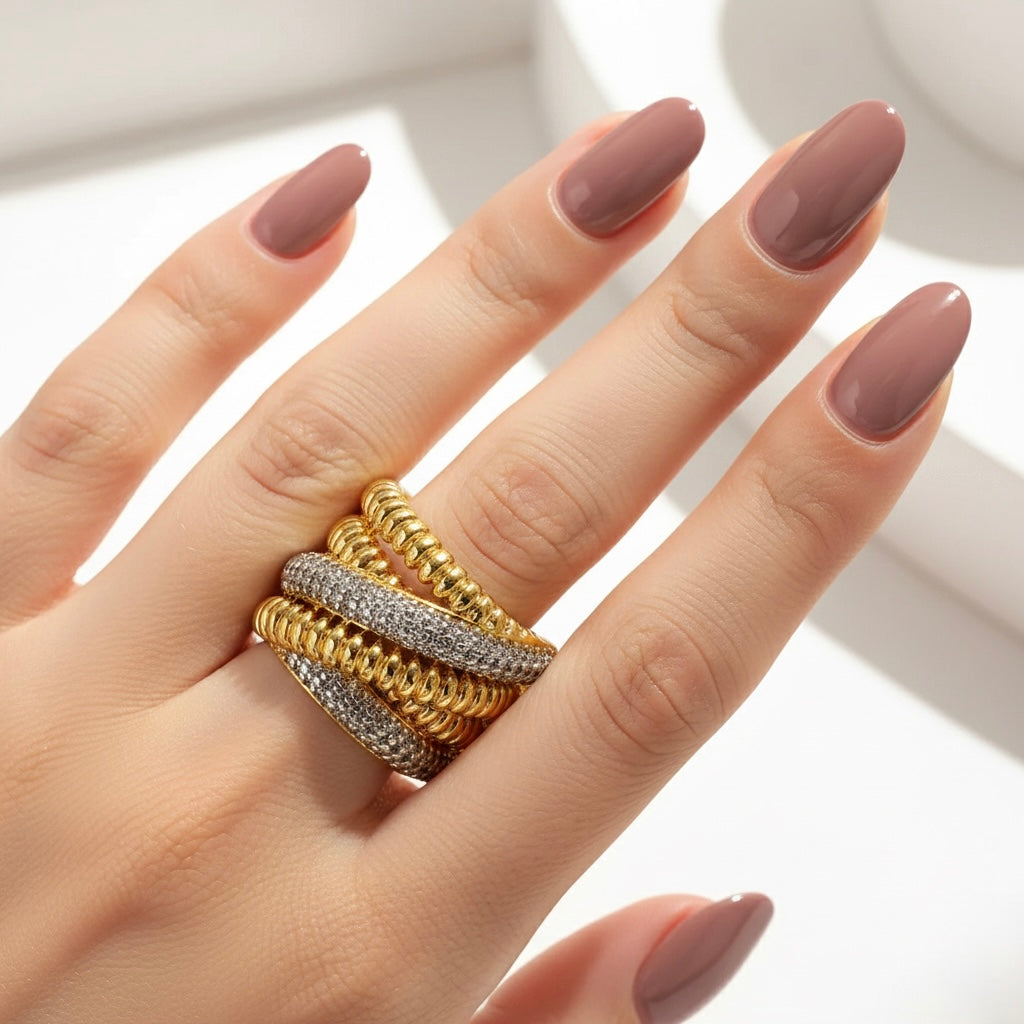 Hand wearing multiple gold rings with a neutral background