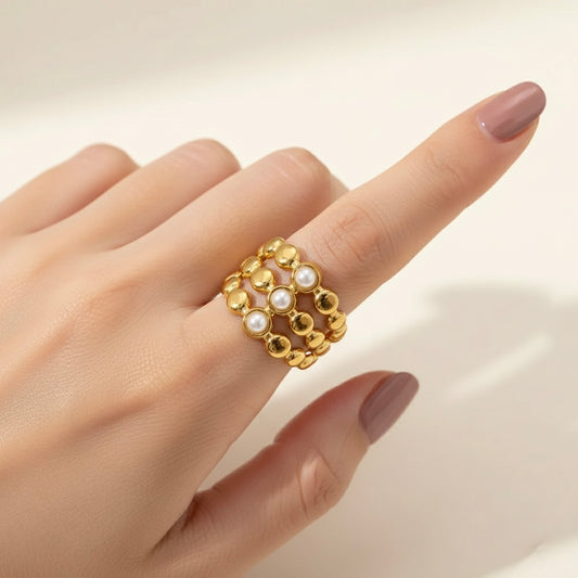 Gold ring with pearls on a hand against a neutral background