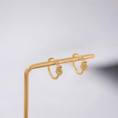 Gold hoop earrings on a gold stand against a light gray background