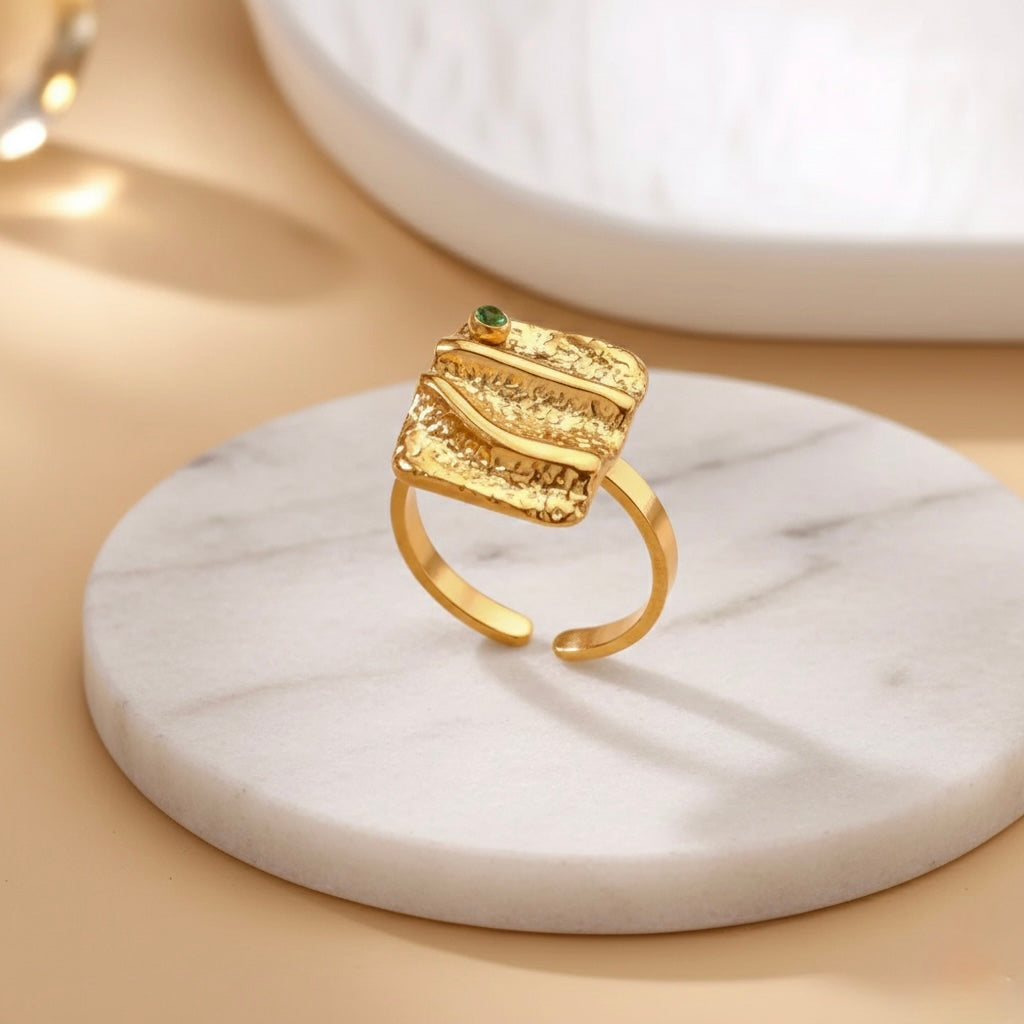 Gold ring with a green gemstone on a marble surface