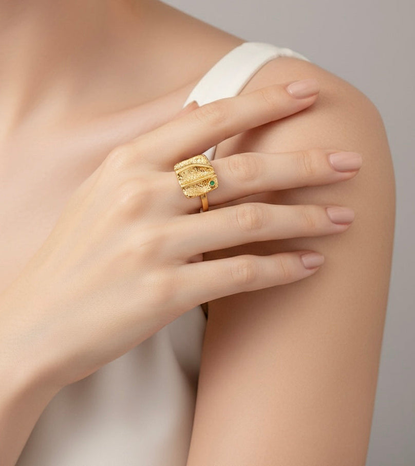 Gold ring with green gemstone on a hand against a neutral background