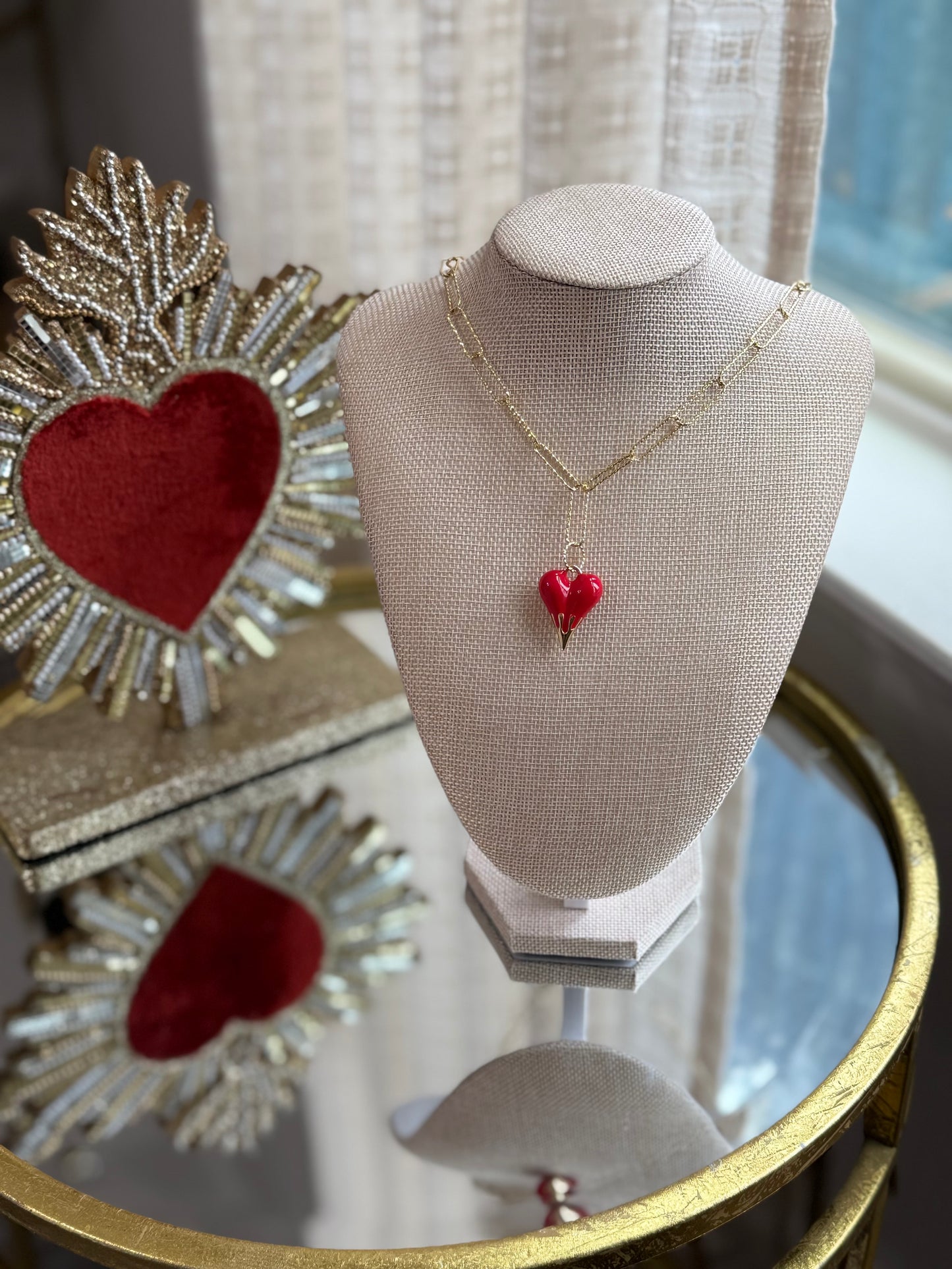 Necklace with a red heart pendant on a mannequin bust, with decorative hearts and a mirror in the background.