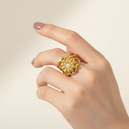 Gold ring with floral design and pearl on a hand against a beige background