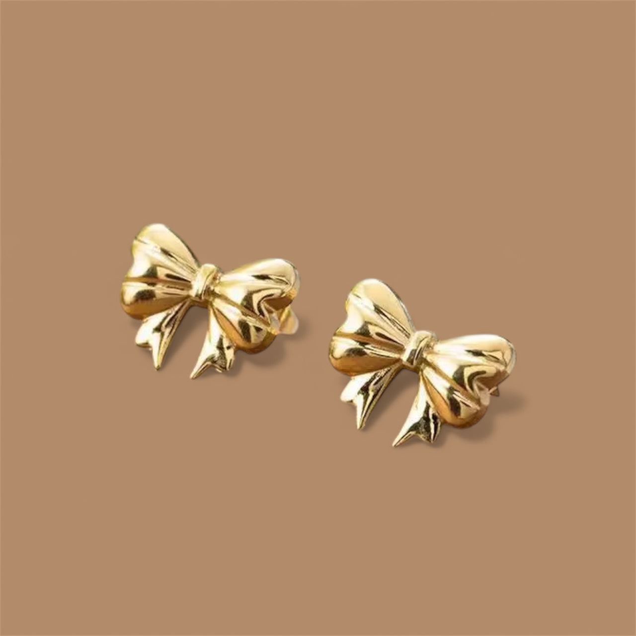 Gold bow-shaped earrings on a brown background