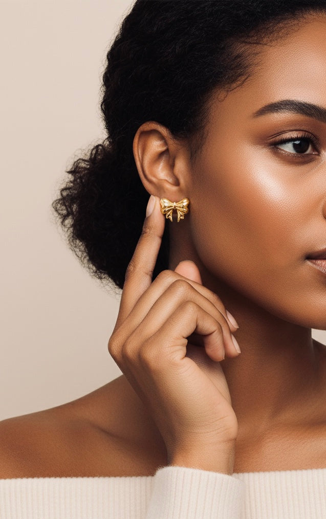 Woman wearing a gold bow-shaped earring on a beige background