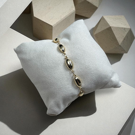 Gold bracelet on a white pillow with geometric stone background
