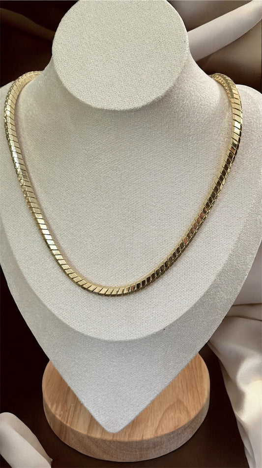 Gold necklace on a white mannequin bust with a brown background
