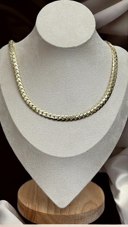 Gold chain necklace on a white bust with a wooden base
