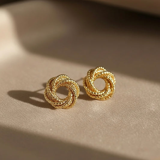 Pair of gold earrings on a beige surface