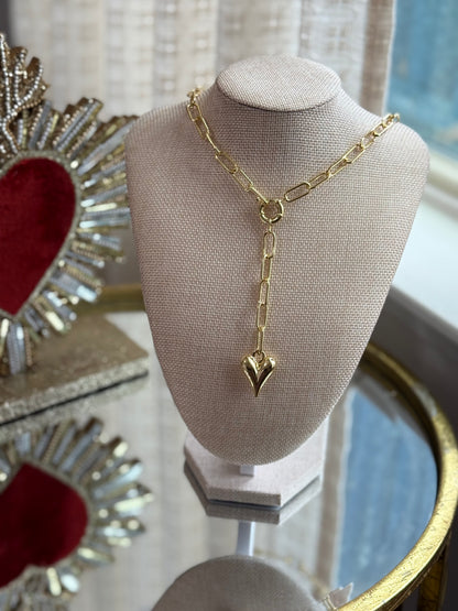 Gold necklace on a mannequin bust with decorative heart-shaped box in the background