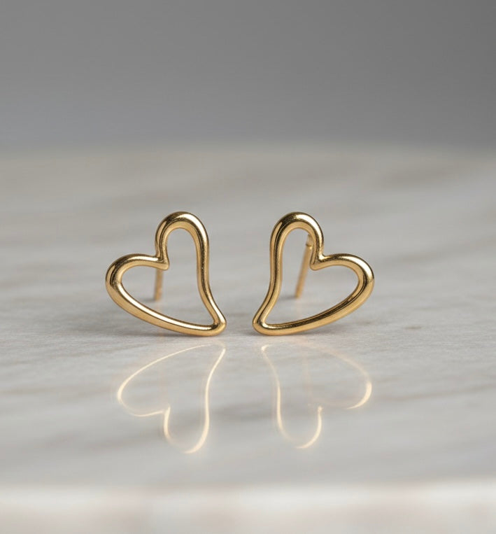 Gold heart-shaped earrings on a reflective surface with a neutral background