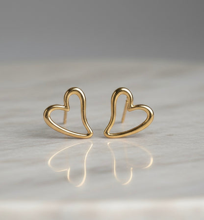 Gold heart-shaped earrings on a reflective surface with a neutral background