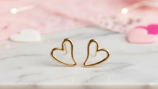 Gold heart-shaped earrings on a marble surface with a soft pink background