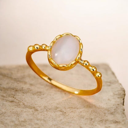 Gold ring with a white stone on a beige background