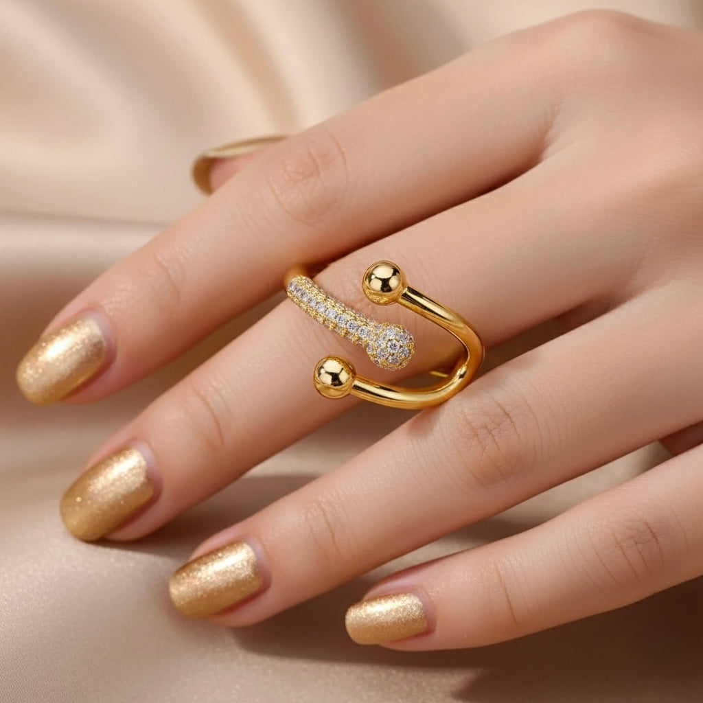Gold ring with a diamond on a hand with gold nail polish against a beige background