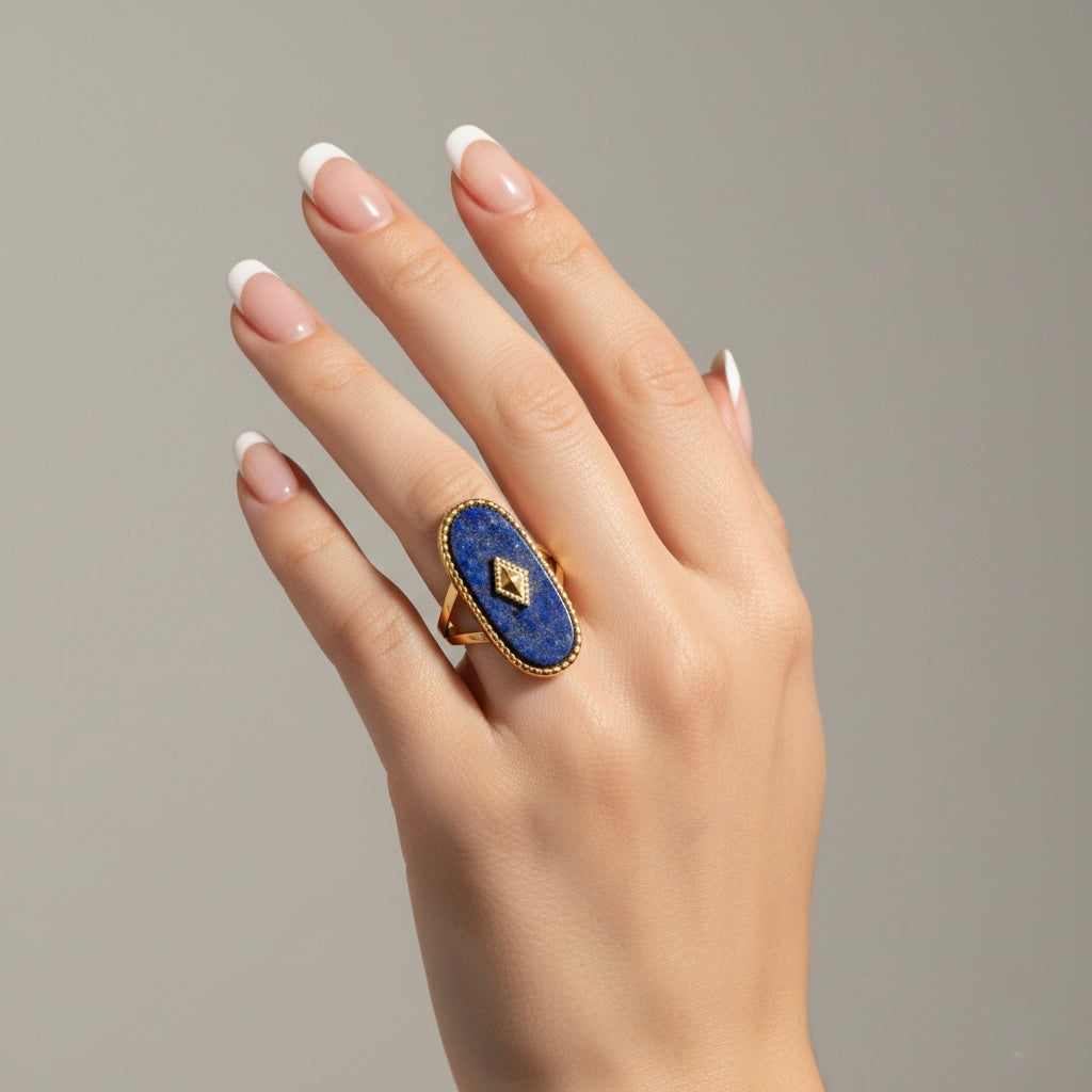 Hand wearing a blue ring with a gold band on a neutral background