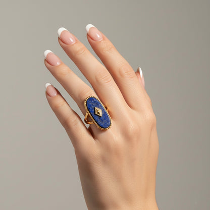 Hand wearing a blue ring with a gold band on a neutral background