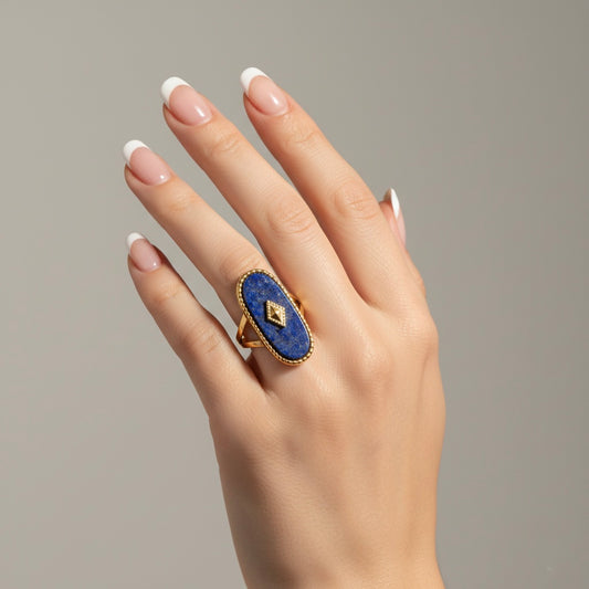 Hand wearing a blue ring with a gold band on a neutral background