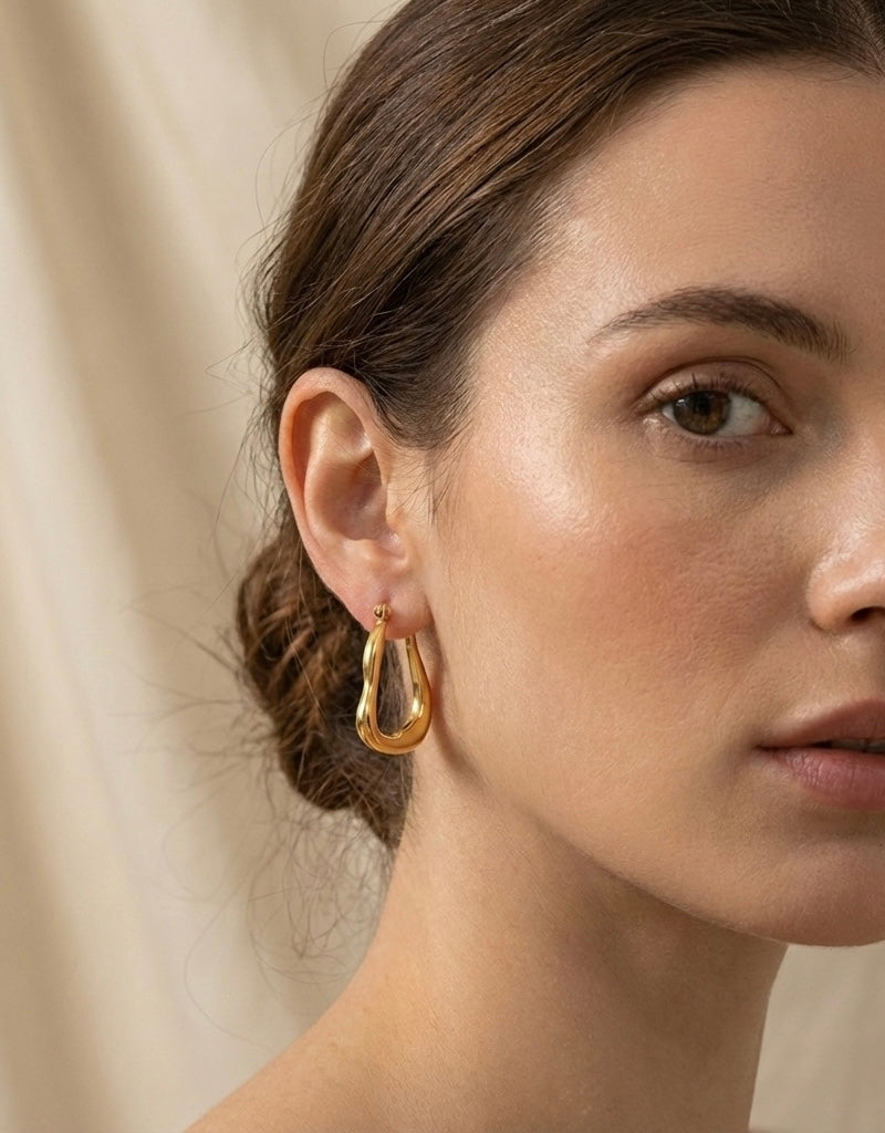 Close-up of a woman wearing gold hoop earrings with a neutral background