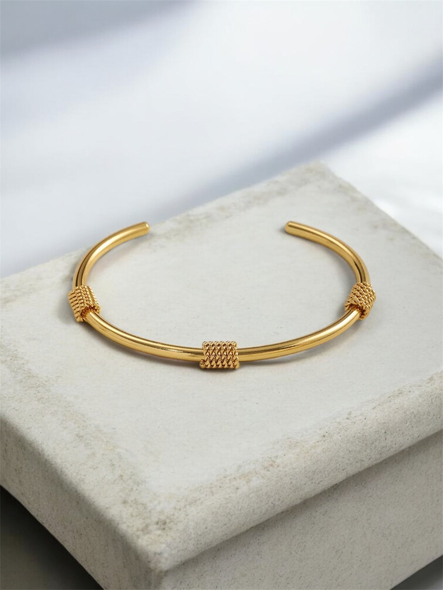 Gold bracelet on a light gray surface with a soft focus background
