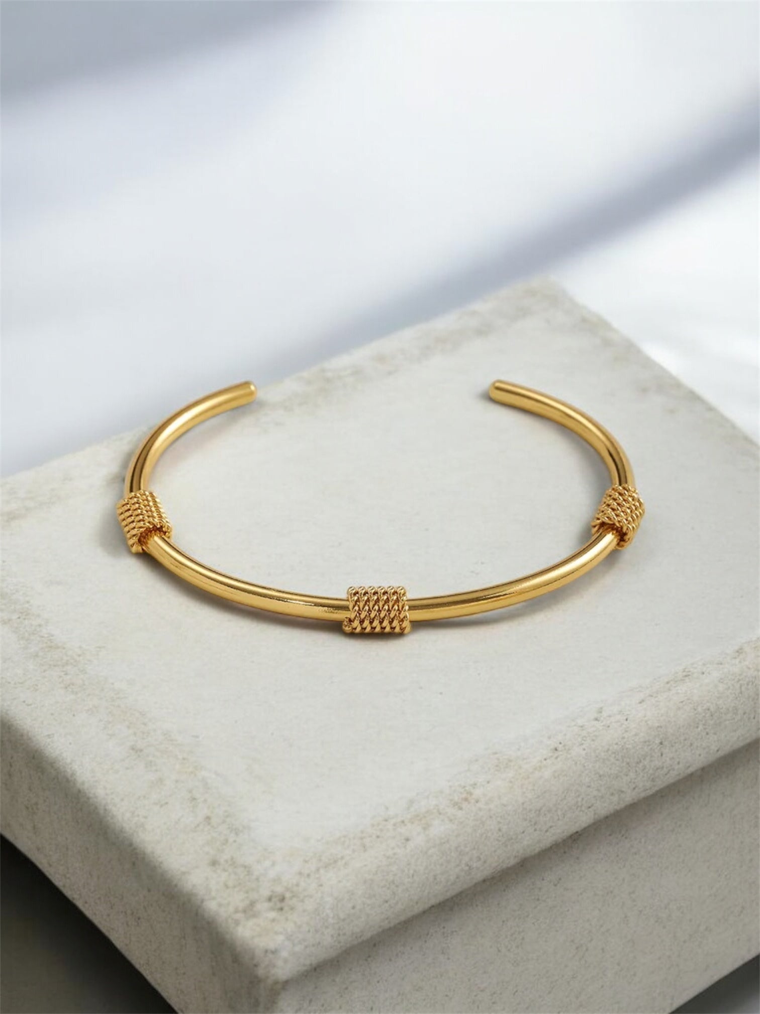Gold bracelet on a light gray surface with a soft focus background