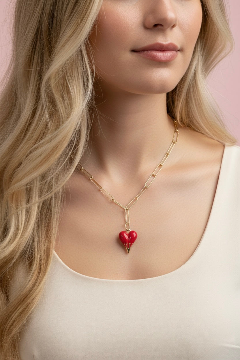 Woman wearing a gold necklace with a red heart pendant against a pink background