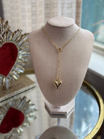 Gold necklace with a heart pendant on a mannequin bust against a decorative background.