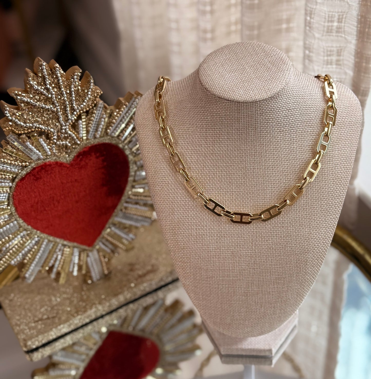 Gold chain necklace on a mannequin bust with decorative heart and leaf item in the background.