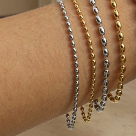 beaded Bracelet, one silver and one gold, draped over a person's arm.