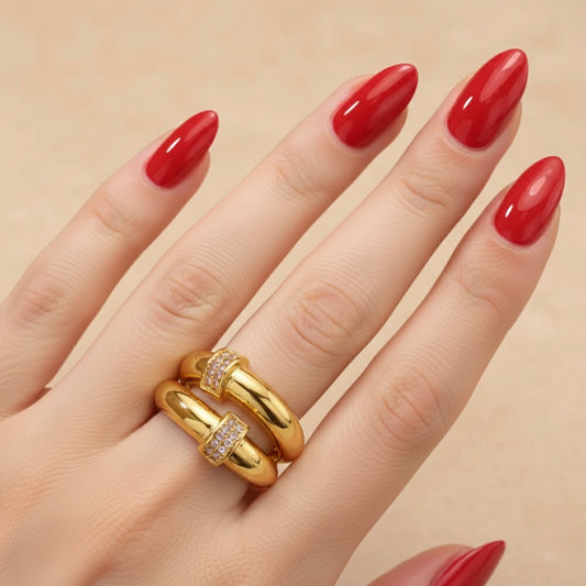 Gold ring on a hand with red nail polish against a beige background
