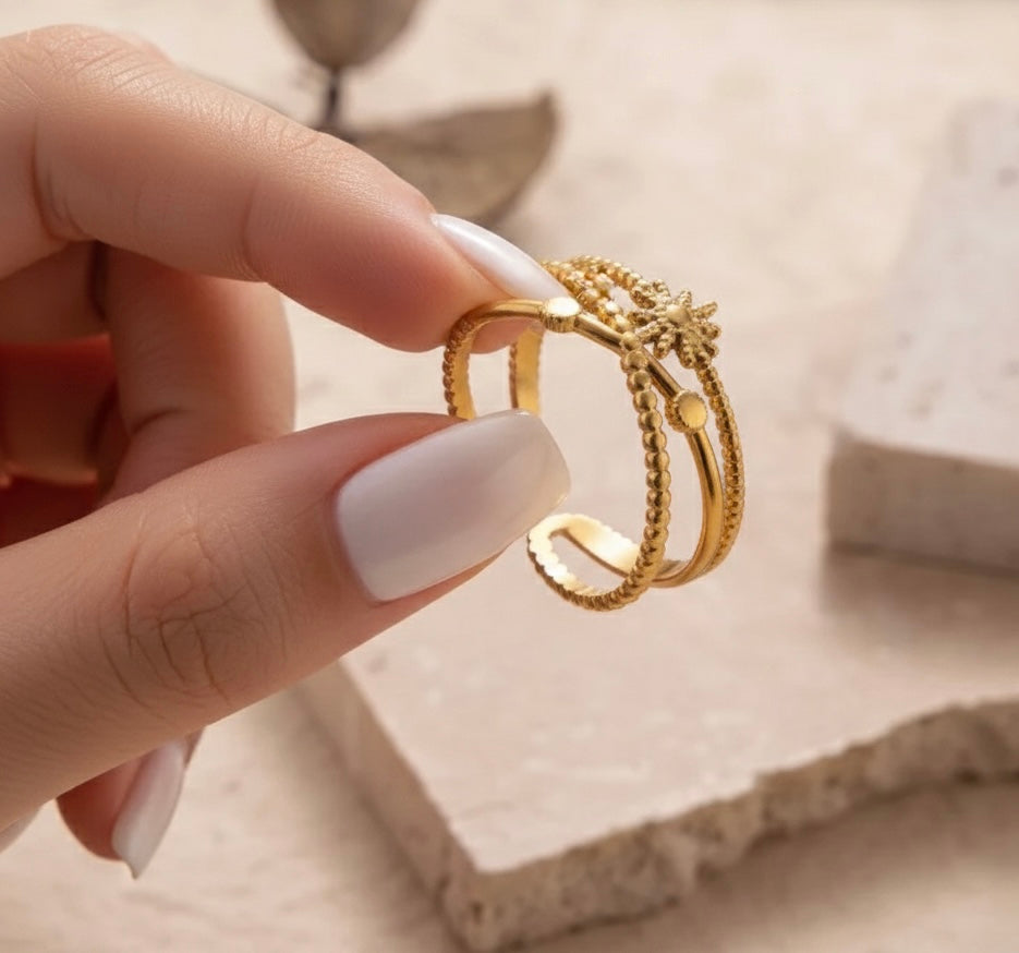 Gold ring held by a hand with light nail polish on a neutral background